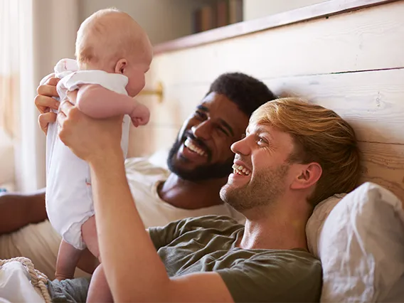 Two fathers holding up their new born baby.