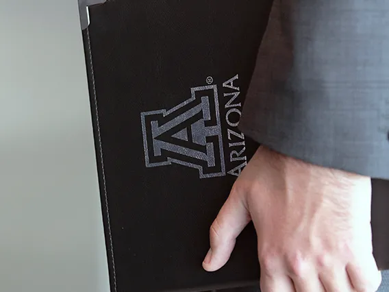 A man in a business suit holding a university of arizona branded portfolio